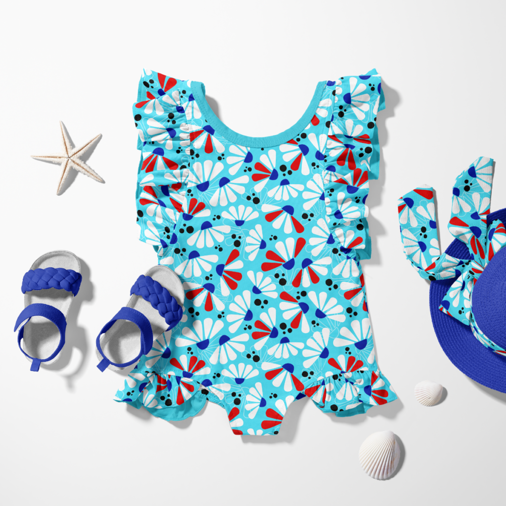 Turquoise floral kids swimsuit styled with blue sandals, a matching sun hat, and seashells.